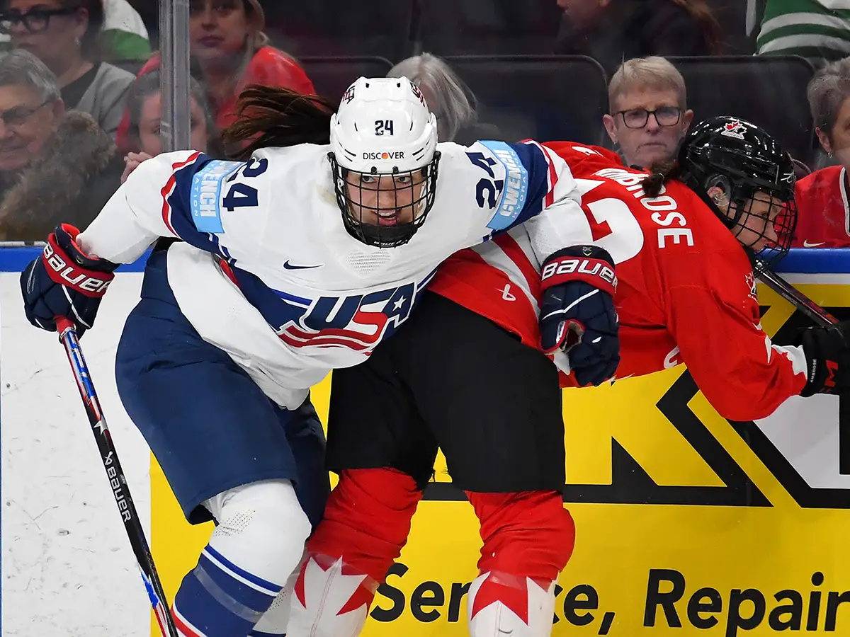 Joy Dunne, a hockey player wearing a Team USA Olympic uniform and pads, checks an opponent into the wall during the 2026 Winter Olympics